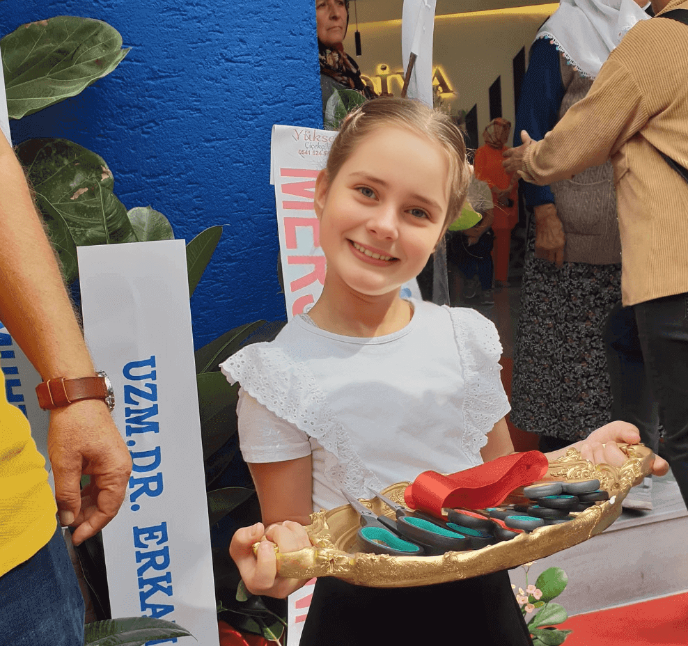 A young girl in a white shirt holding a tray of toothbrushes and smiling at an event